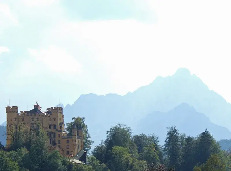 The beautiful medieval style castle of Hohenschwangau in front of Alpine peaks in the sunshine